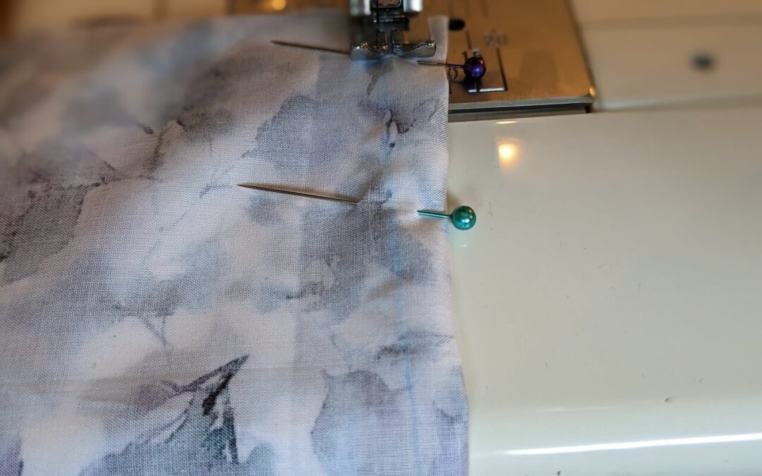 A floral piece of fabric with pins in it sits on a sewing machine, ready for stitching.